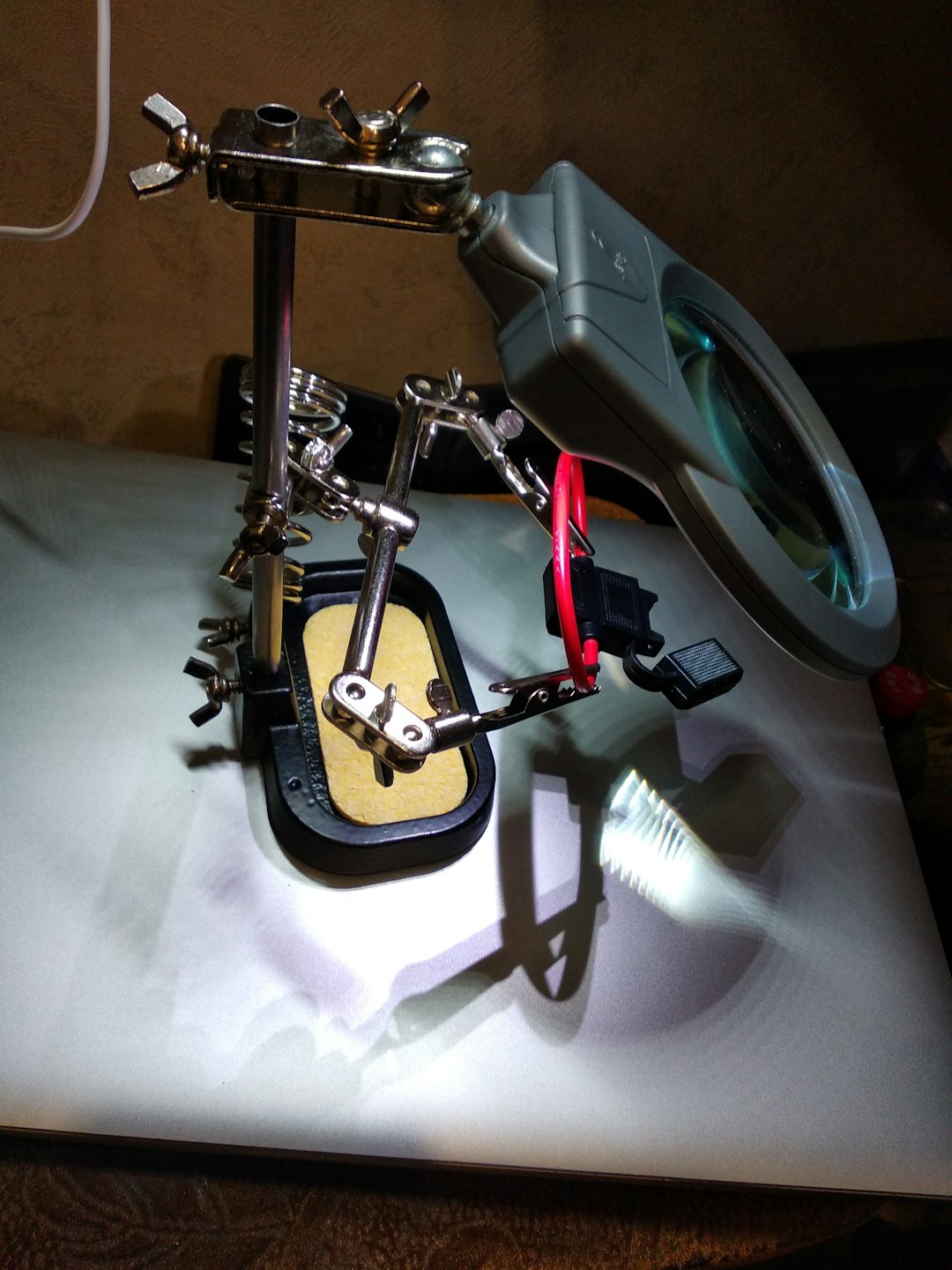 Helping hands tool with clamps and magnifying glass for electronics repair.