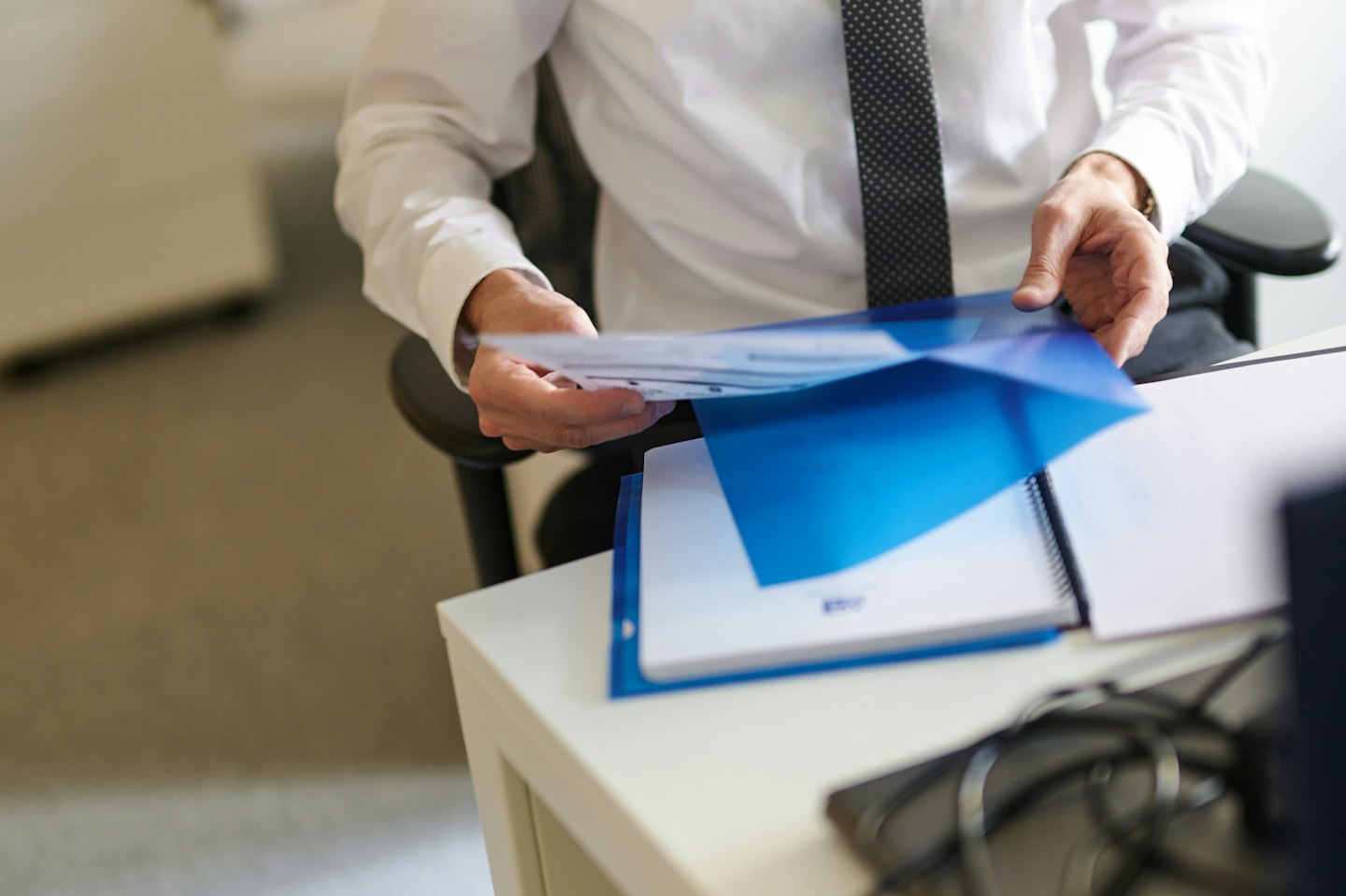 Person organizing papers in a blue folder at a desk.