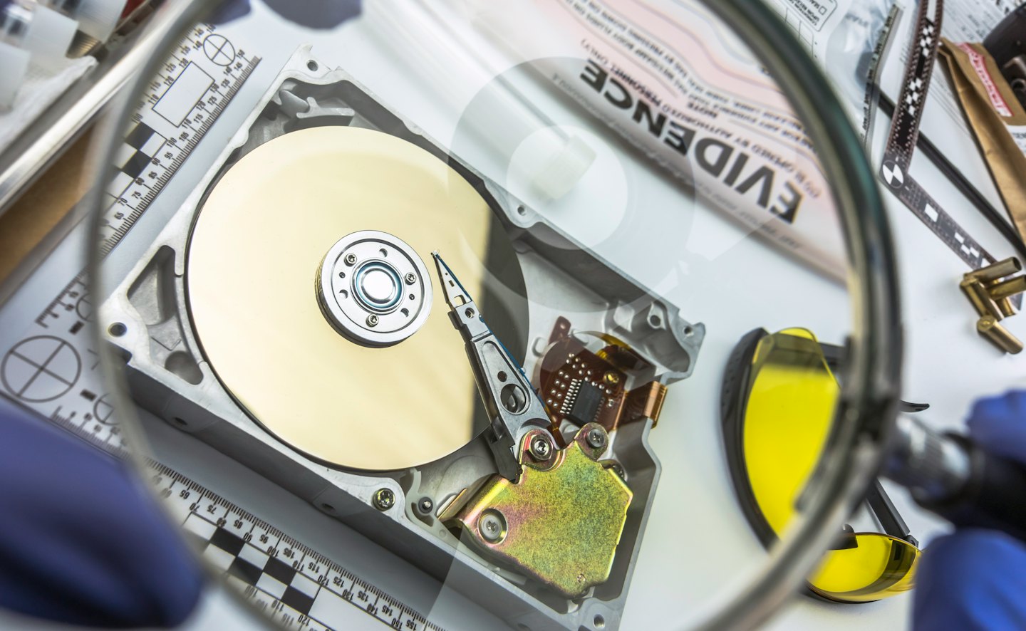 A technician inspects a computer hard drive using a magnifying glass.